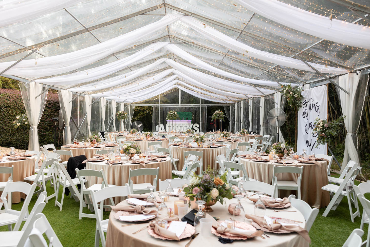 Tables set with dishes under a large white tent for a wedding reception