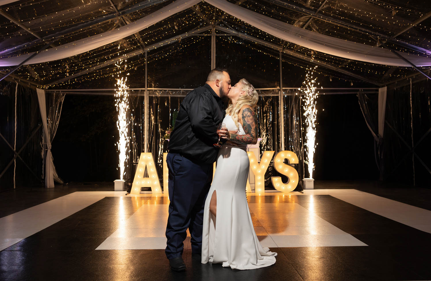 Bride and groom kissing in front of a large lit up sign saying "always"