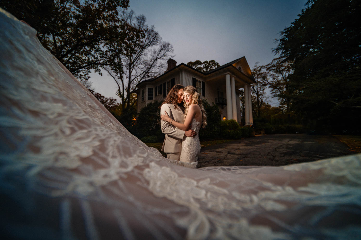 A bride and groom, holding hands and gazing into each other's eyes, stand on the steps of the historic Duncan Estate.