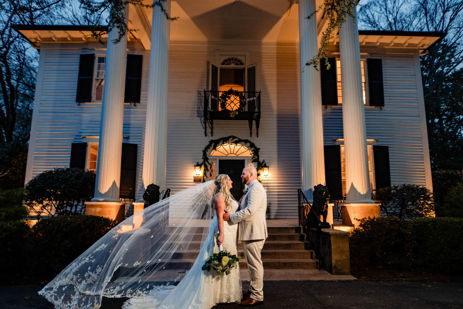 bride and groom standing outside Duncan Estate at night with veil blowing in the wind