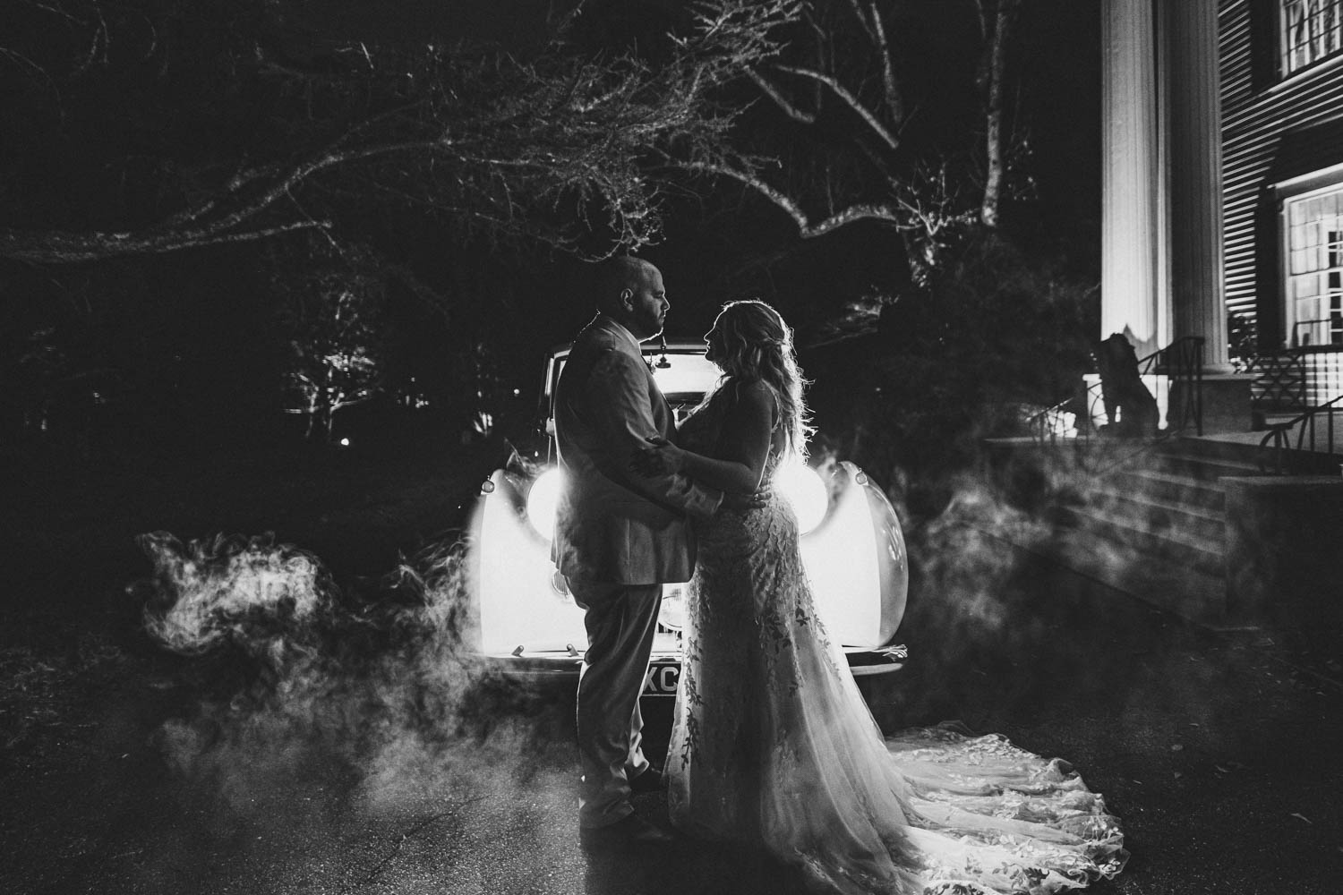 couple holding hands in front of an old car with headlights on