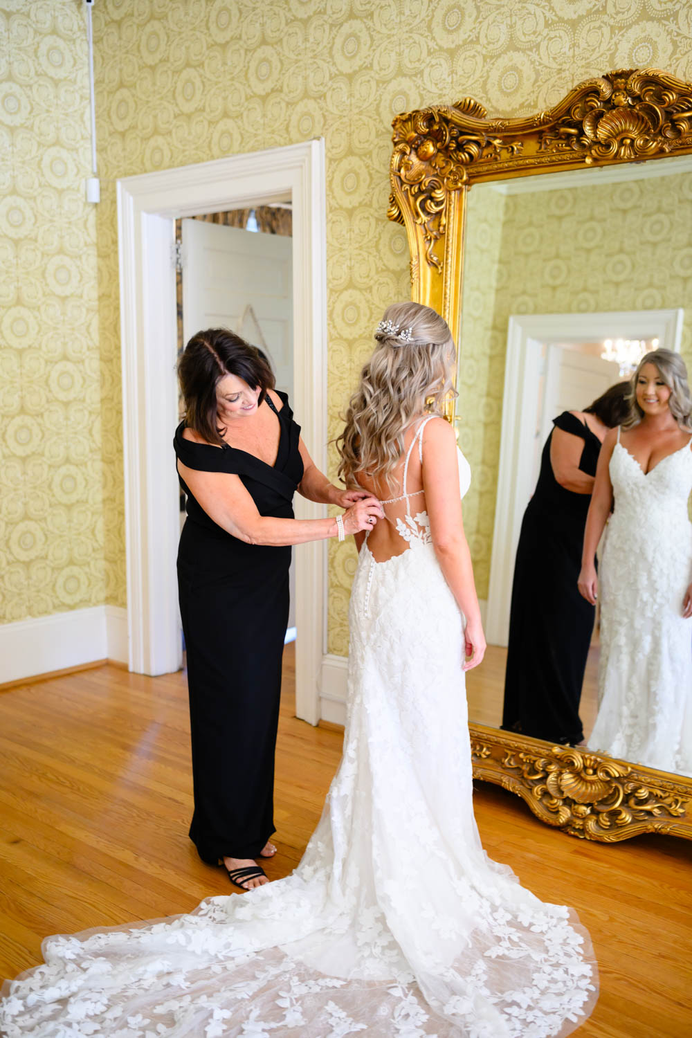 Mother helping her daughter button her wedding dress