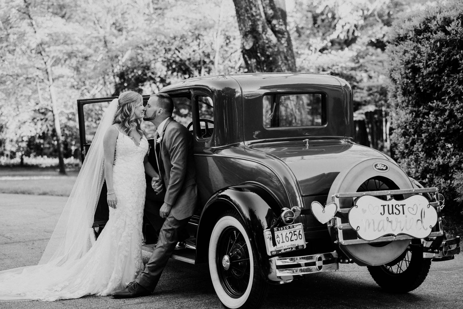 A couple leaning against an old car after their wedding