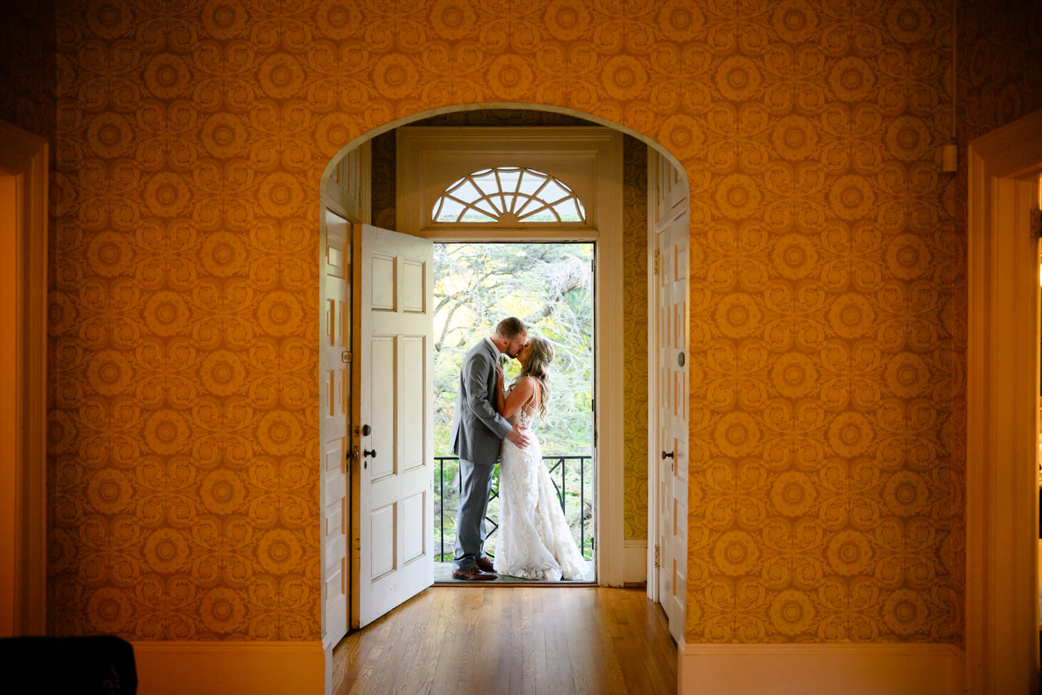 Bride and groom kissing in a doorframe with sunlight shining through