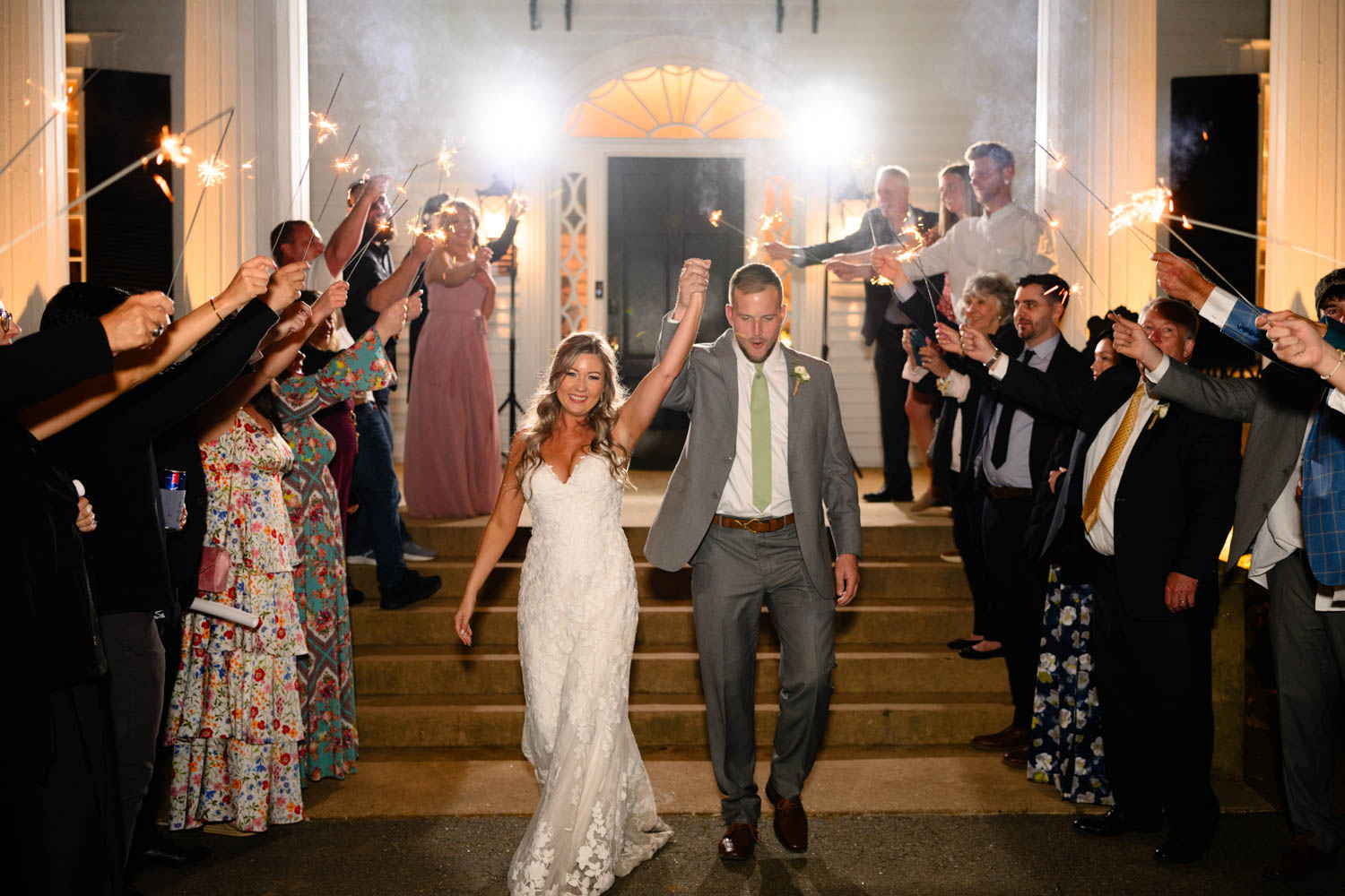 A couple leaving their wedding holding their hand in the air with friends behind them