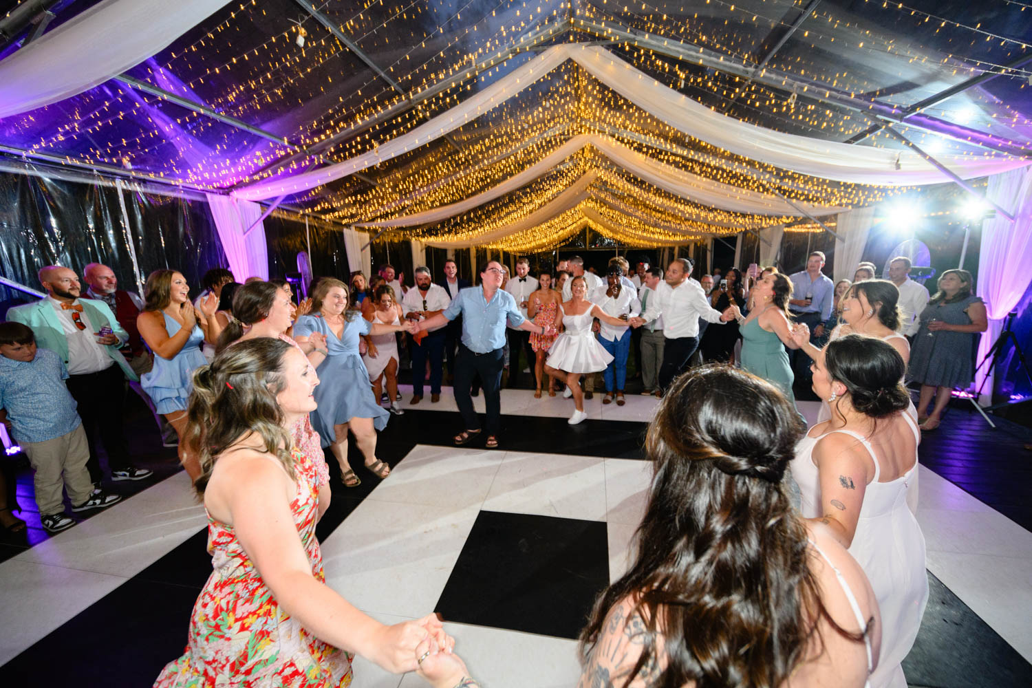 Large group of friends dancing at a wedding reception under a tent