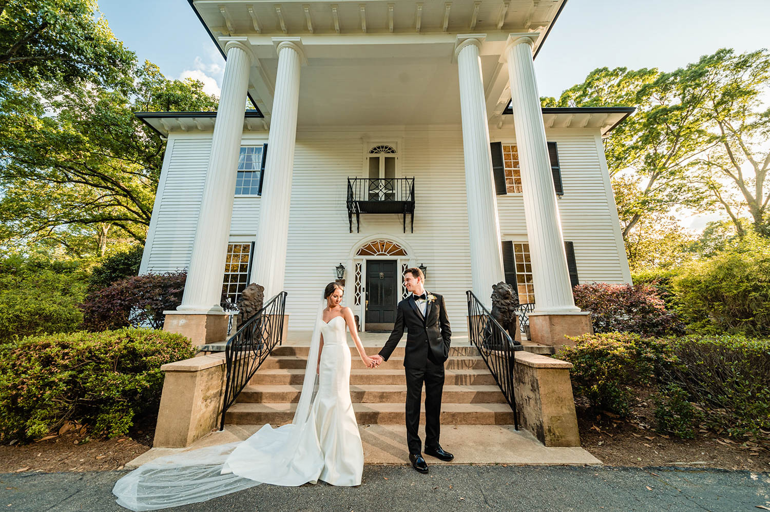 Bride and groom standing in front of a white estate house